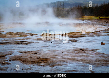 Ausbruch des Geysir mit Felsen, Pool und dampfende Rückstände im zentralen Dorf von Geysir in Island Stockfoto