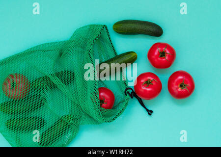 Frische Gurken und Tomaten aus Shopping net fallen. Reife Gemüse flach Ansicht von oben. Gesunde vegetarische Ernährung. Gewachsene natürliche Produkte. Salat Zutaten auf blauem Hintergrund. Einfache wallpaper Stockfoto