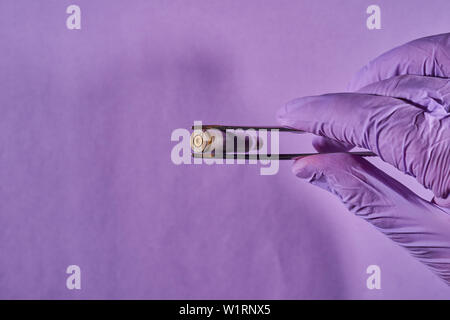 Die behandschuhte Hand mit Pinzette und bullet Gehäuse. Stockfoto