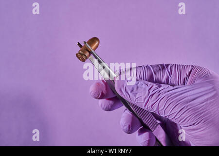 Die behandschuhte Hand mit Pinzette und bullet Gehäuse. Stockfoto