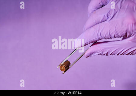 Die behandschuhte Hand mit Pinzette und bullet Gehäuse. Stockfoto