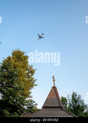 Landsitz von Gorki, Moskau, Russland - 20. Juni 2019: Orthodoxes Kreuz und Flugzeug. Orthodoxe Kirche aus Holz und ein Passagierflugzeug in den Himmel fliegen Stockfoto