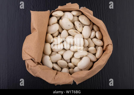 Bean in Papiertüten auf dem Küchentisch. Lebensmittelzutaten, die in der Küche verwendet. Der dunkle Hintergrund. Stockfoto