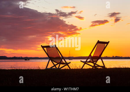 Zwei Sonnenliegen und Boote im letzten Abendlicht am Chiemsee Strand in Epenwöhrden Stockfoto