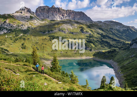 Ein Mann und eine Frau wandern über den Salvar Insee, rote Wand im Hintergrund, lechweg, Lech Quelle Berge, Vorarlberg, Österreich Stockfoto