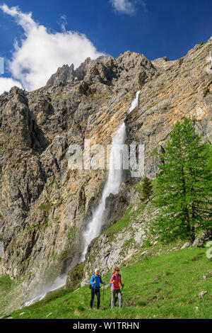 Mann und Frau wandern aufsteigend in Richtung Hütte Rifugio Stroppia, Wasserfall Cascata Stroppia im Hintergrund, Val Maira, Cottischen Alpen, Piemont, Italien Stockfoto