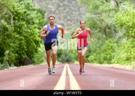 Bestimmt der Mann und die Frau, die auf der Straße gegen Bäume. Läufer sprintete in voller Länge sportlich männlich und weiblich sind in Sportbekleidung. Sportliche Läufer Fitness Sport paar Training unter. Stockfoto