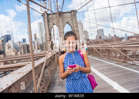 Gerne asiatische Frau mit Phone sms Wandern auf der Brooklyn Bridge, New York City für Social Media oder bloggen. Touristische tun Sommer Reisen in Manhattan, USA. Stockfoto