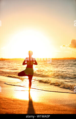 Meditation Frau üben Vriksasana Baum yoga Pose am Strand bei Sonnenuntergang. Serene junger Erwachsener Silhouette in Morgensonne flare balancing Meditation eine Body Workout. Wellness Konzept.
