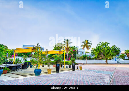 Kleiner Strand Restaurant in gelben Farbtönen auf dem Bürgersteig, umgeben von Grün. Von Muscat, Oman. Stockfoto