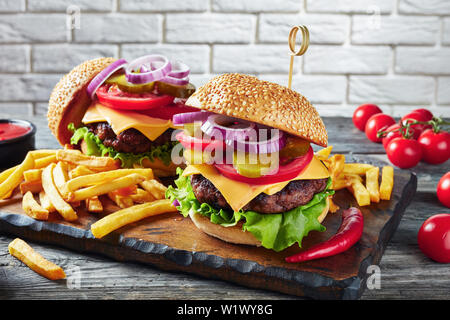 Hamburger mit Cheddar Käse, frisch gebackene Brötchen, gebratenes Rindfleisch Burger, Gurken, Salat, Ketchup, Senf, Zwiebeln, Tomaten und Pommes frites auf Stockfoto