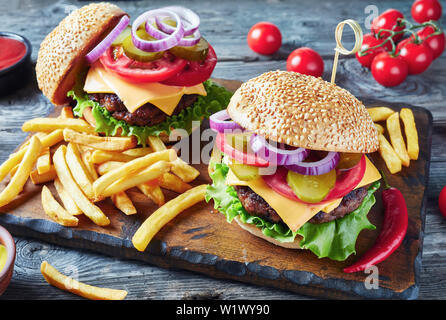 Hamburger mit Käse, gerösteten Brötchen, gebratenes Rindfleisch Burger, Gurken, Salat, Ketchup, Senf, Zwiebeln, Tomaten und Pommes frites auf einem schneiden Boar Stockfoto