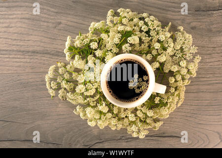 Flach Schuß von Kaffee in weiße Tasse mit weißen Blumen. Cowparsley und heiße Getränke auf hölzernen Tisch. Horizontale Foto. Stockfoto