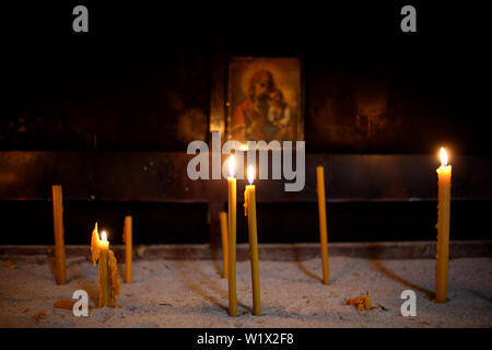 Brennende Kerzen in der orthodoxen Kirche auf dem Hintergrund der Ikone der Gottesmutter. Stockfoto