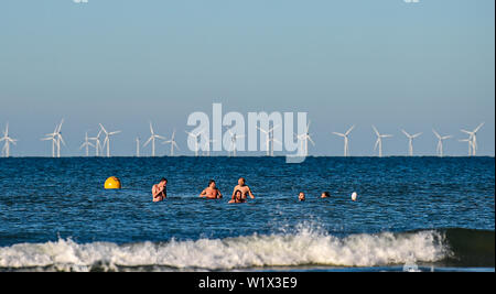 Brighton UK 4. Juli 2019 - Am frühen Morgen Schwimmer tauchen Sie ein in das Meer aus Brighton Beach mit den Rapunzeln Wind Farm hinter in der Ferne genießen. Das Wetter wird prognostiziert einen weiteren sonnigen Tag an der Südküste von Großbritannien mit zu erwartenden Höchsttemperaturen um 27 Grad in einigen Teilen zu erreichen. Foto: Simon Dack/Alamy leben Nachrichten Stockfoto
