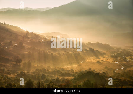 Atemberaubende Herbst Landschaft Sonnenaufgang im Lake District mit Sonnenstrahlen Streaming durch den Nebel in die langdales Tal Stockfoto