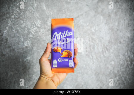Milka Schokolade in der Hand halten, auf den grauen und weißen Hintergrund. Stockfoto