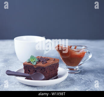 Ein Stück leckere hausgemachte Schokolade Kuchen auf den Teller mit Puderzucker, minzblatt und Schokolade Löffel auf grauem Hintergrund Stockfoto
