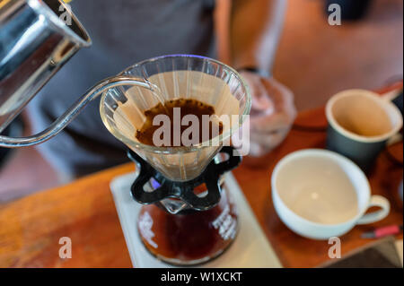 Barista strömenden heißen Wasser in Papierfilter mit Kaffeepulver auf Becher Stockfoto