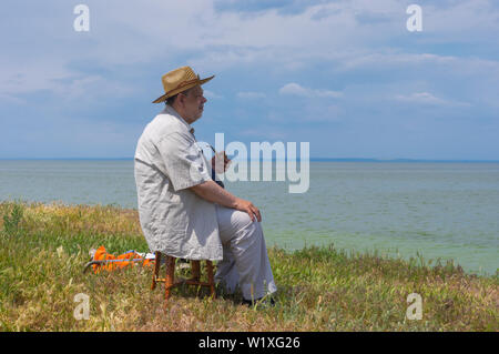 Einsame ältere Mann sitzt auf einem Hocker am steilen Ufer des Dnjepr River, Ukraine Stockfoto