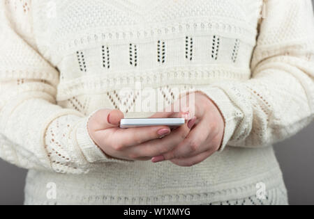 Mädchen schaut auf den Bildschirm des Smartphones. Gepflegte Finger mit einer Maniküre. Kein Gesicht, halten Sie das Handy in den Händen. Stockfoto