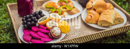 BANNER, LANGE FORMAT Frühstück auf einem Tablett mit Obst, Brötchen, Avocado Sandwiches, smoothie Schüssel stehen auf dem Gras Stockfoto