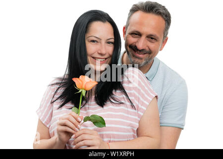 Fröhlicher Mann und Frau Paar umarmen mit orange Rose als Geschenk auf weißem studio Hintergrund isoliert Stockfoto
