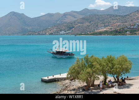 Insel Spinalonga, Kreta, Griechenland. Juni 2019. kleine Passagier Fähre Transport von Touristen nach Spinalonga eine ehemalige Kolonie für Leprakranke. Hintergrund der Festland Cr Stockfoto