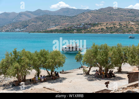 Insel Spinalonga, Kreta, Griechenland. Juni 2019. kleine Passagier Fähre Transport von Touristen nach Spinalonga eine ehemalige Kolonie für Leprakranke. Hintergrund der Festland Cr Stockfoto