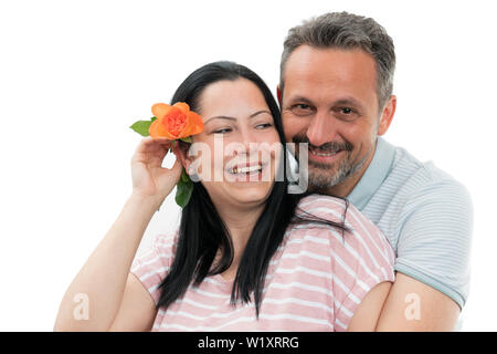 Freudiger Mann umarmt glücklich Frau mit orange Rose hinter dem Ohr als Paar Geschenk Konzept auf weißem Hintergrund Stockfoto