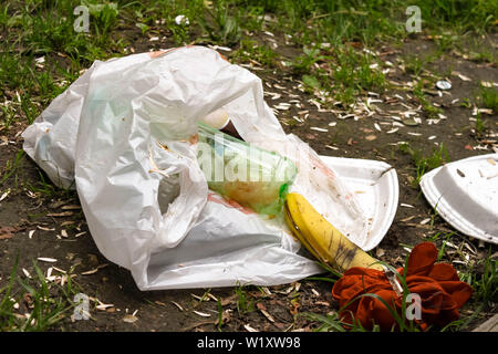 Zerknitterte Plastiktüte mit Müll und Wegwerf Utensilien auf dem Rasen im Park in der Nähe. Umweltverschmutzung. Müll, Dump, Kunststoffabfällen Verschmutzung Stockfoto