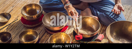 Frau spielen auf Tibetische Klangschale sitzend auf Yoga Matte gegen einen Wasserfall. Vintage tonned. Schöne Mädchen mit mala Perlen meditieren BANNER Stockfoto