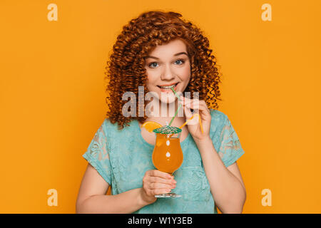 Sommer frischen Cocktail. Nettes Mädchen mit Curly Frisur trinken orange Cocktail auf Sommer orange Hintergrund Stockfoto