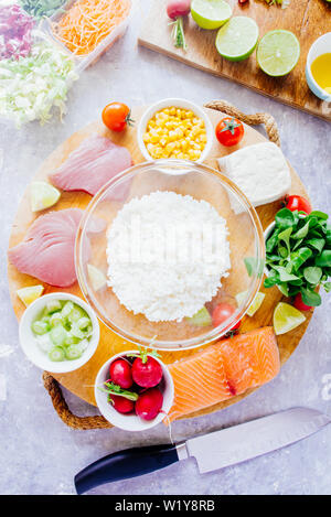 Poke Schüssel sind te letzte Trend in der Lebensmittelindustrie, eine Schüssel mit Gemüse und Lachs auf einem gelb rosa Hintergrund mit riesigen monstera Blatt um. Stockfoto