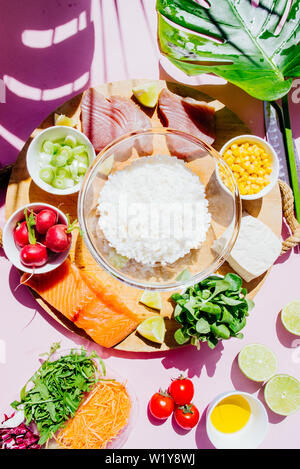 Poke Schüssel sind te letzte Trend in der Lebensmittelindustrie, eine Schüssel mit Gemüse und Lachs auf einem gelb rosa Hintergrund mit riesigen monstera Blatt um. Stockfoto