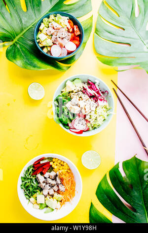 Poke Schüssel sind te letzte Trend in der Lebensmittelindustrie, eine Schüssel mit Gemüse und Lachs auf einem gelb rosa Hintergrund mit riesigen monstera Blatt um. Stockfoto