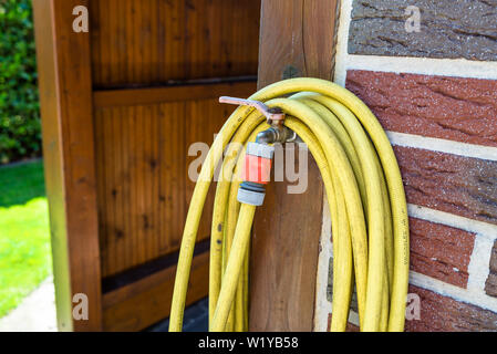 Ein Garten gelben Schlauch an einem Tippen ragen aus dem Bauernhof Gebäude vor dem Hintergrund der Backsteinfassade verbunden, ein Foto Nahaufnahme. Stockfoto