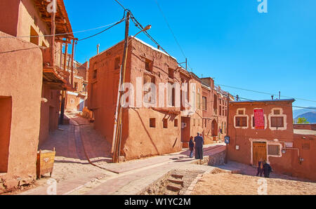 ABYANEH, IRAN - 23. OKTOBER 2018: die hügeligen Straßen des Dorfes mit traditionellen adobe Häusern gesäumt sind, mit rotem Ocker Schlamm bedeckt, das ist Besuch Auto Stockfoto