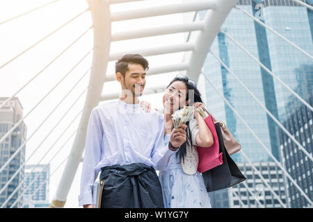 Geschäftsmann holding Dollar cash mit Laptop und asiatische Frau mit einkaufskorb sind glücklich lächelnd in die Stadt Stockfoto