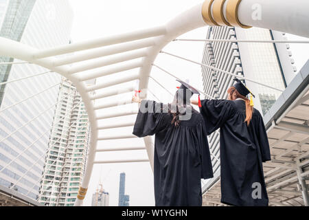 Zwei junge Frauen in akademischen Kleid Hand heben mit Erfolg Bachelor der Universität Stockfoto