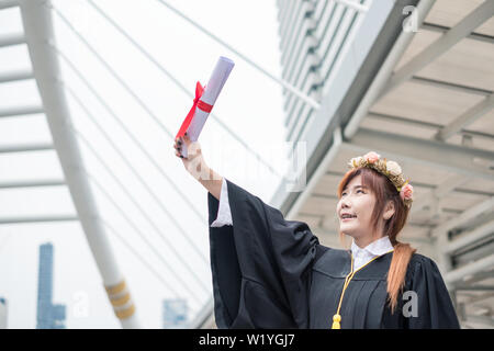 Frau mit akademischen Kleid Hand heben mit Erfolg Bachelor der Universität Stockfoto
