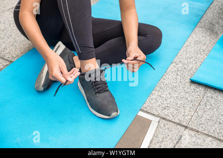Frau in Sportbekleidung sitzen Riegel schuhbändern auf Blue mat Stockfoto