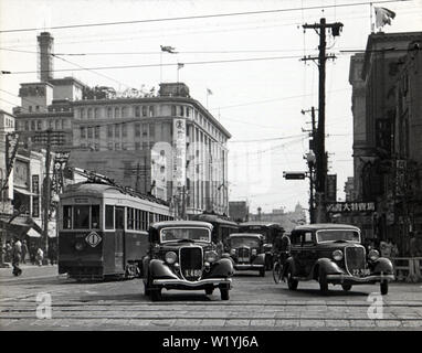 [1930er Jahre Japan - Nihonbashi, Tokyo] - Autos und Straßenbahnen auf Chuodori in Nihonbashi im Mai 1934 (Showa 9). Der Fotograf machte dieses Foto von der Kreuzung der Chuodori und Eitai-dori. Das Gebäude auf der Rückseite des Hotels ist Takashimaya Kaufhaus. 20. Jahrhundert vintage Glas schieben. Stockfoto