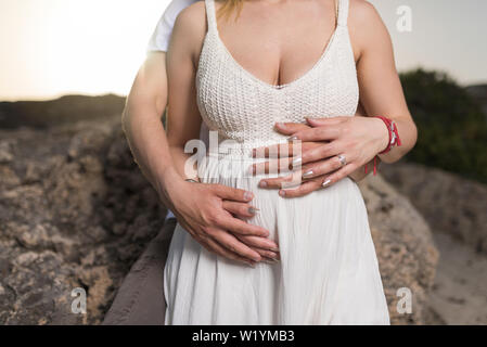 Mann mit Bauch der seine schwangere Frau. Schwangere und liebevoller Ehemann umarmen Bauch am Strand. Stockfoto