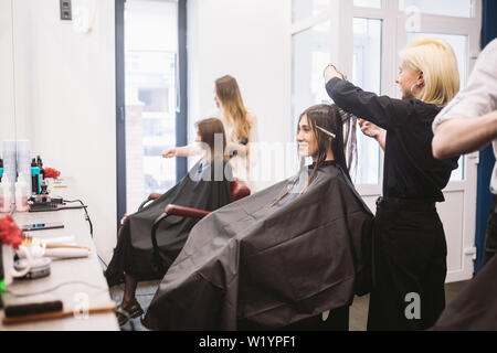 Friseur holding Schere und Kamm und macht Haarschnitt Frau Client. Junge schöne Frau die Haare schneiden im Beauty Salon. Prozess der Haare schneiden mit verwenden Stockfoto