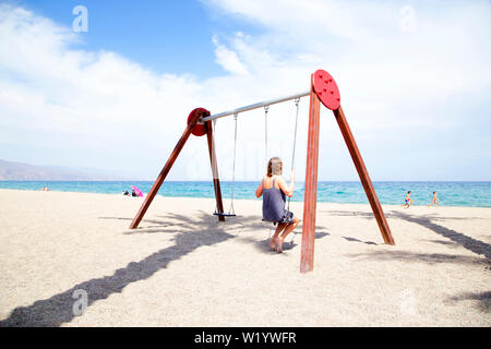 Frau mittleren Alters auf einer Schaukel sitzend. Am Strand mit der Sonne auf ihrem Gesicht. Stockfoto