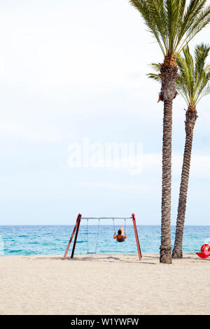 Frau mittleren Alters Schwingen auf einer Schaukel. Am Strand mit der Sonne auf ihrem Gesicht. Stockfoto