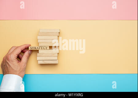 Hand ein Geschäftsmann einen Stapel Spielsteine aus Holz mit einem Schild Strategie auf einer von ihnen. Über bunte Papier Hintergrund. Stockfoto