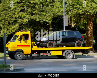 Schwarzes Auto ist entweder auf einen gelben Abschleppwagen auf einer Straße der Stadt an einem Sommertag geladen. Wieder aus dem Auto. Das Leben in der Stadt. Stockfoto