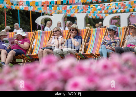 Die Menschen saßen in Liegestühlen geniessen der Musik im musikpavillon an der RHS Hampton Court Flower Show 2019. Hampton Court Palace, East Molesey, Surrey, Englan Stockfoto